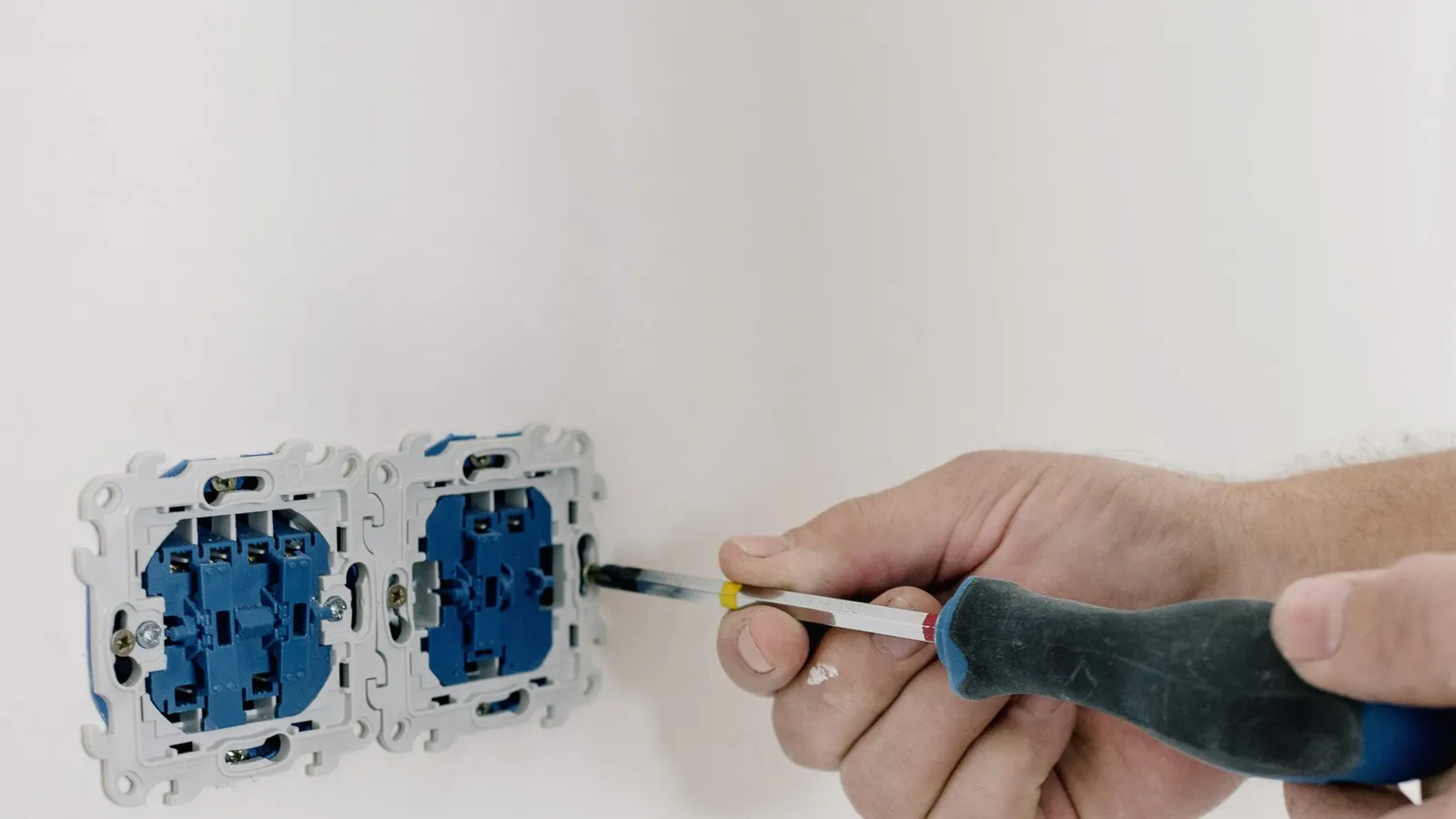Close de uma mão instalando uma tomada elétrica na parede, com uma chave de fenda