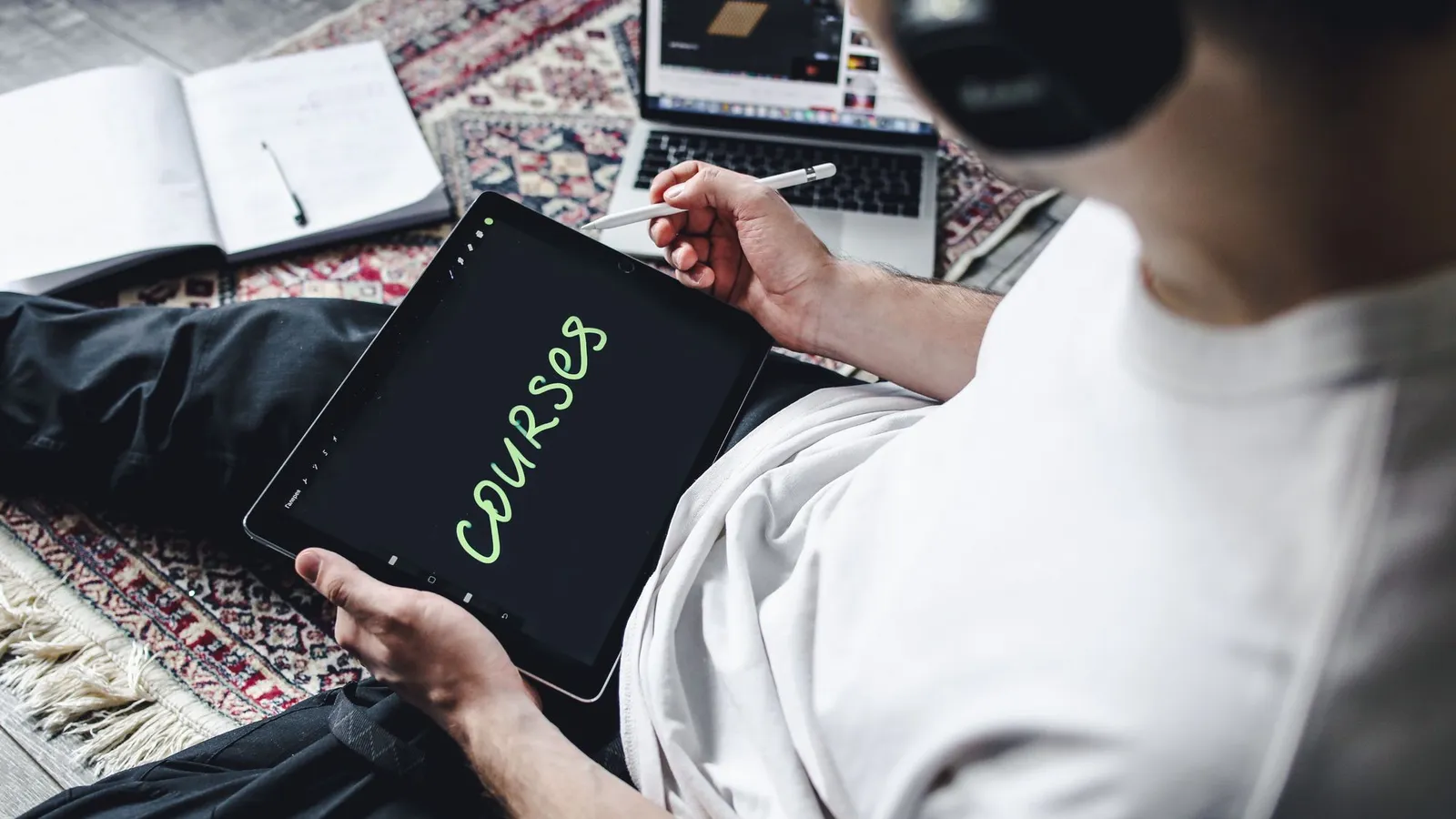 Pessoa sentada no chão, estudando um curso online num tablet com caneta digital