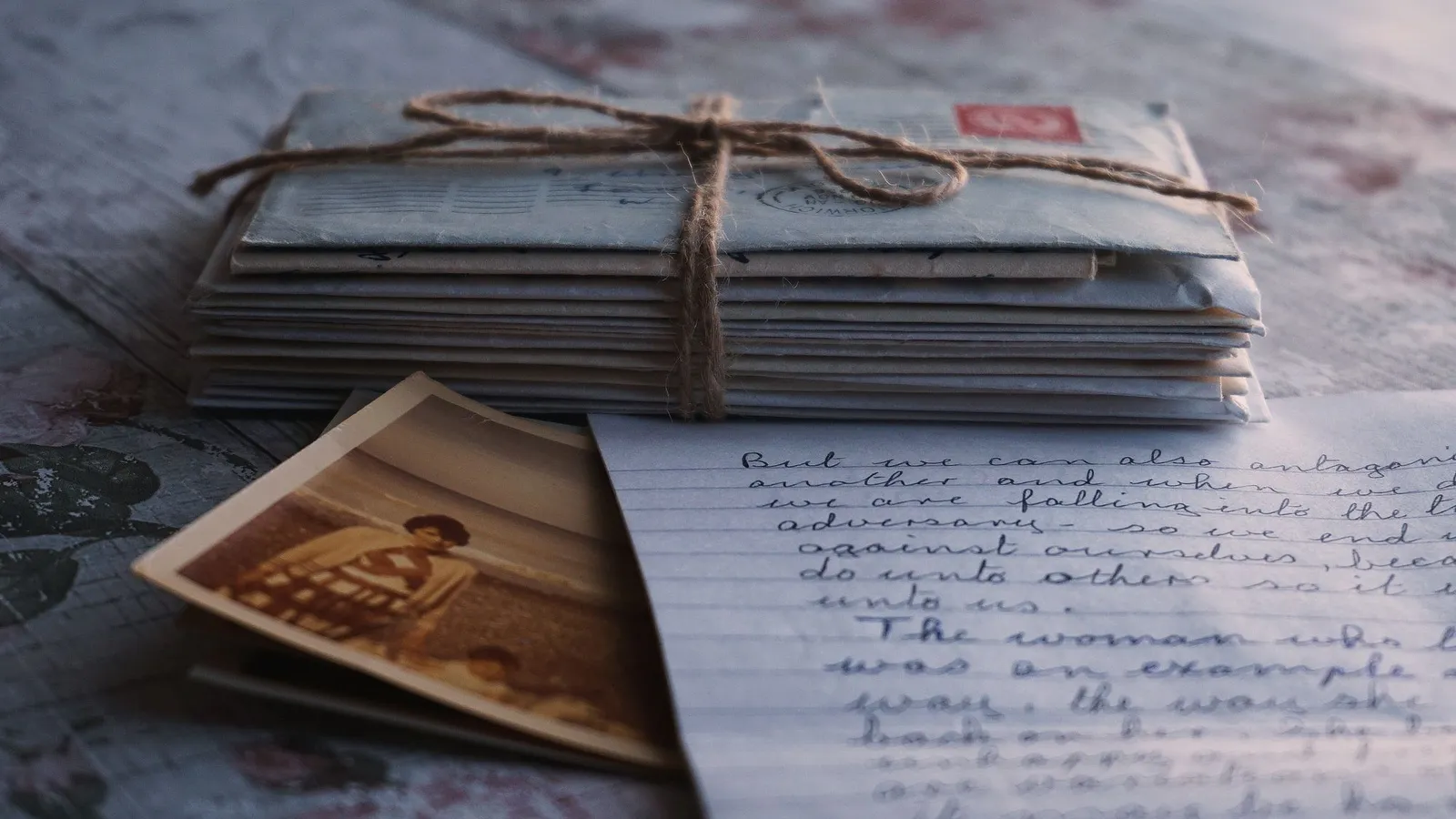 Cartas e fotografias antigas amarradas com barbante, sobre uma mesa de madeira