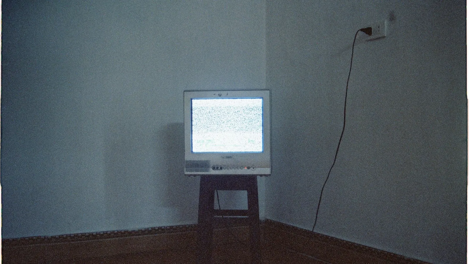 Televisão de tubo antiga, ligada, exibindo apenas estática, num cômodo escuro